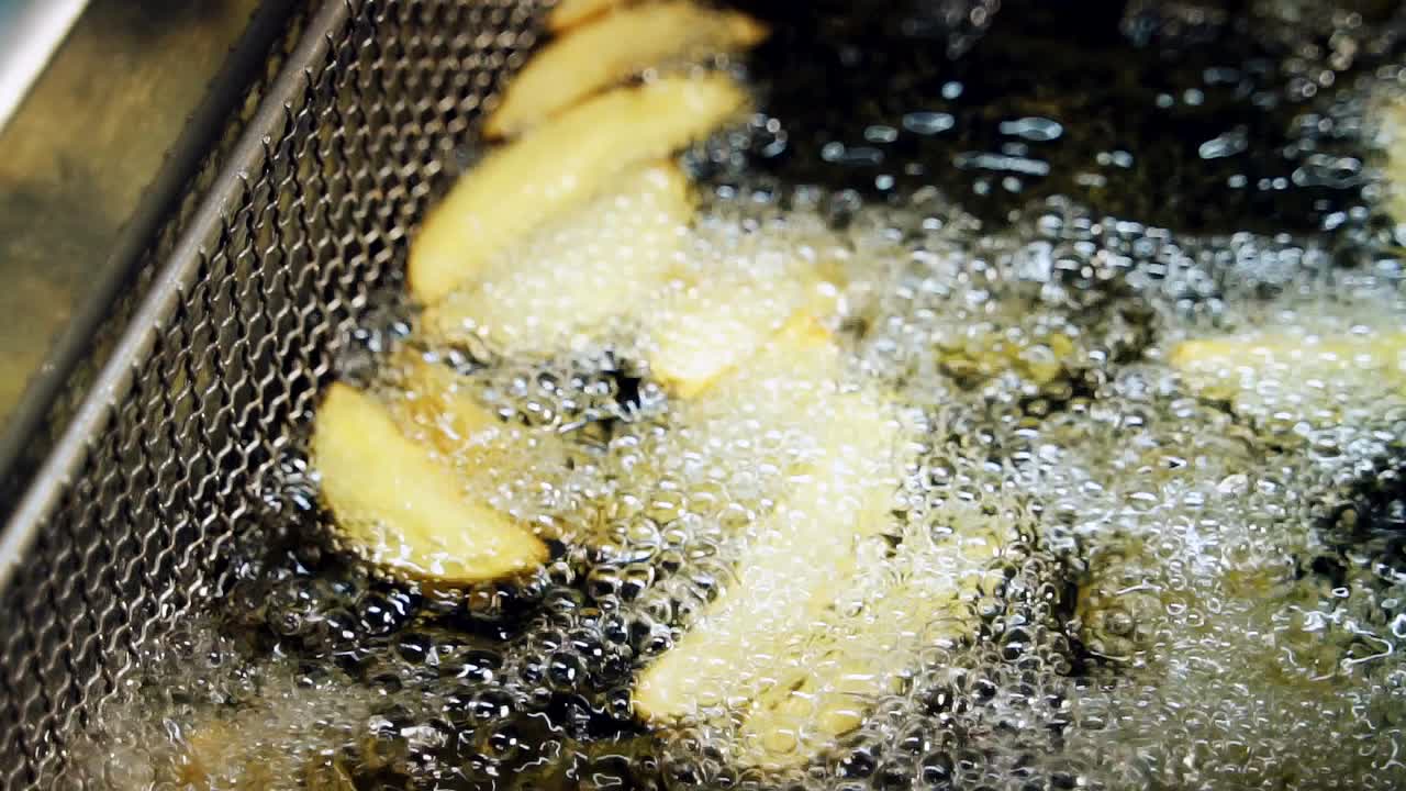 Preparation of french fries in deep fryer with a lot of boiling oil in the restaurant, slow motion