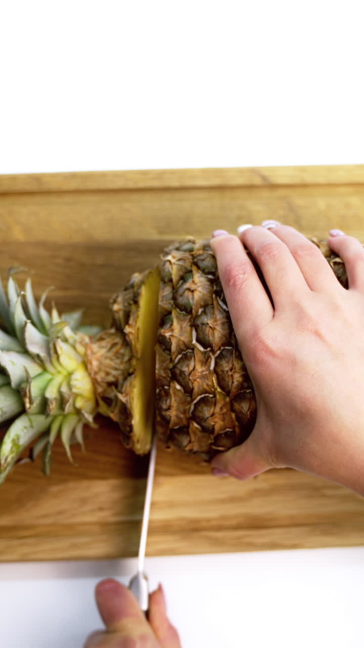Pineapple against white background. Slicing ripe pineapple with sharp knife on table