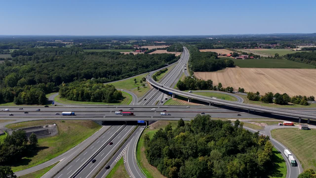 Junction of Germany autobahn highway during sunny day. New build freeway interchange with curvy street and exits. Suburb district in summer. Forest landscape and trucks on interstate. Drone wide shot