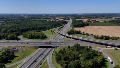 junction of germany autobahn highway during sunny day. new build freeway interchange with curvy street and exits. suburb district in summer. forest landscape and trucks on interstate. drone wide shot
