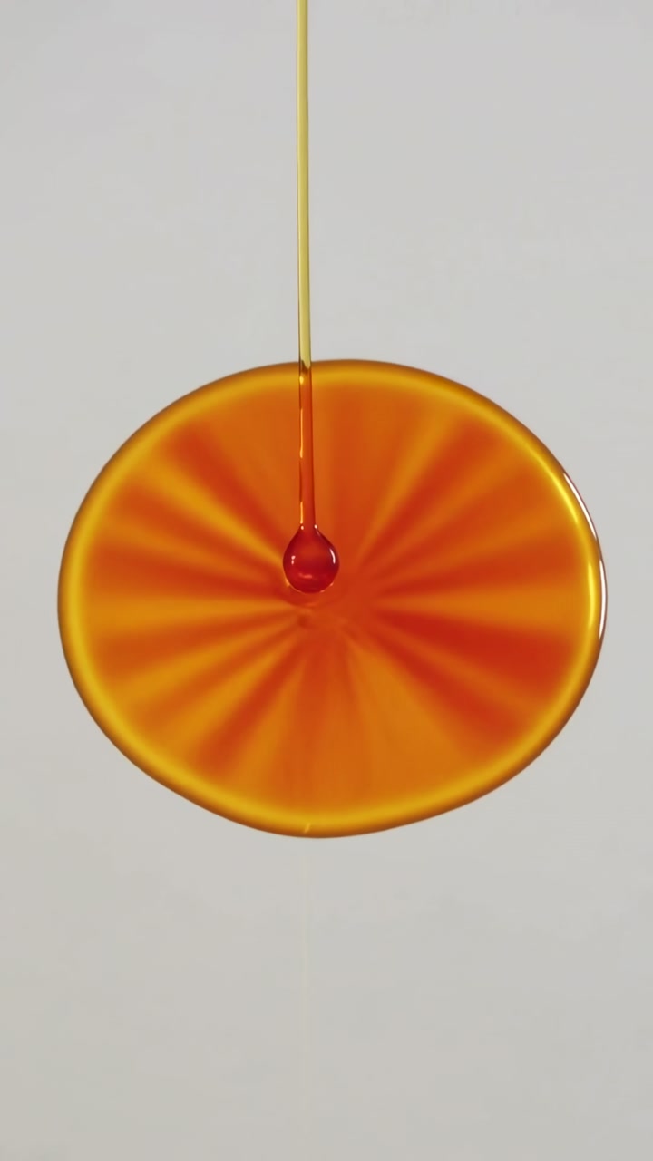 Vertical video: Pouring amber stream from top forming hanging drop, radial disk on light-gray wall