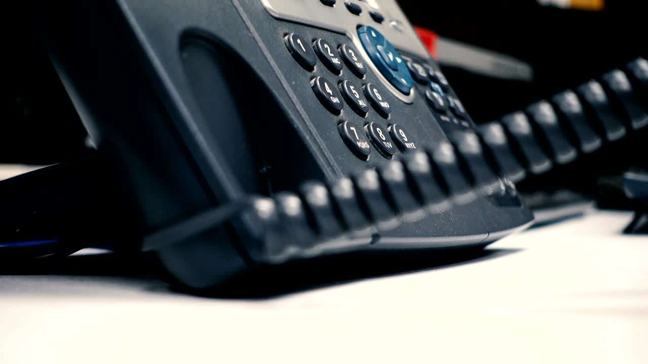 la mano recoge el teléfono negro, marca un número y cuelga, contra el fondo de una sala de computadoras de la oficina. profundidad de campo poco profunda.