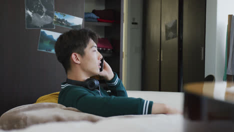 asian boy talking on smartphone sitting on the couch at home