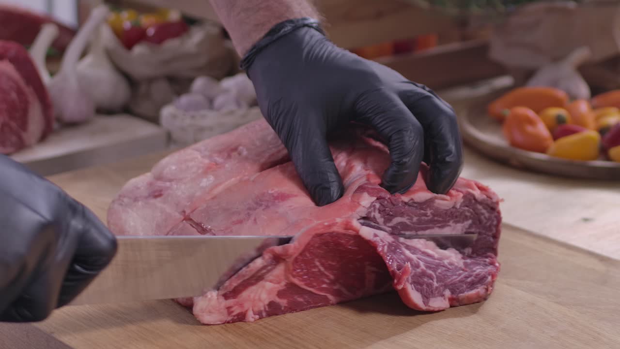 Primo piano di un macellaio professionista che taglia abilmente spesse bistecche di costolette di manzo da un arrosto di manzo crudo fresco su un tagliere di legno