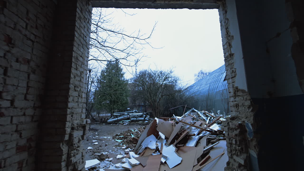 Wet snow falling on the yard filled with the piles of debris. Entering through the wide doorway a spacious room with bare brick walls.