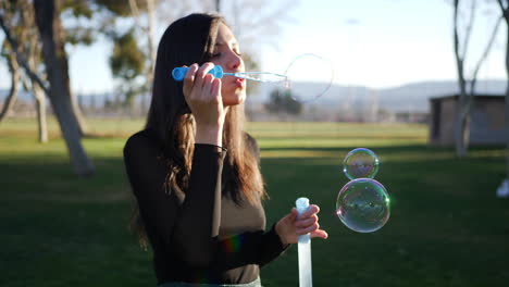 feliz joven hispana soplando burbujas de ensueño flotando bajo el sol brillante al aire libre con lentes en cámara lenta