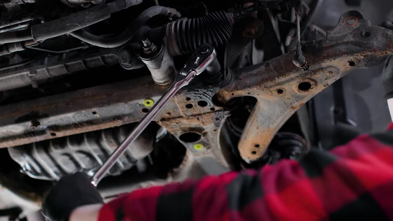Close up of mechanic loosening a suspension bolt under a car with a breaker bar ratchet wrench. Static shot in 4k.