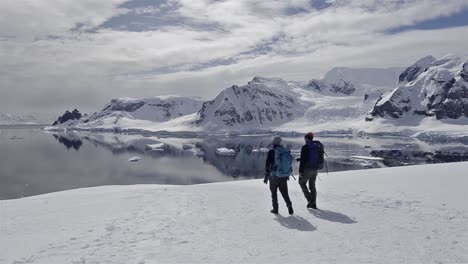 Panning-motion-from-two-hikers-to-a-Gentoo-penguin-colony-in-snow-on-Danco-Island-in-Antarctica-