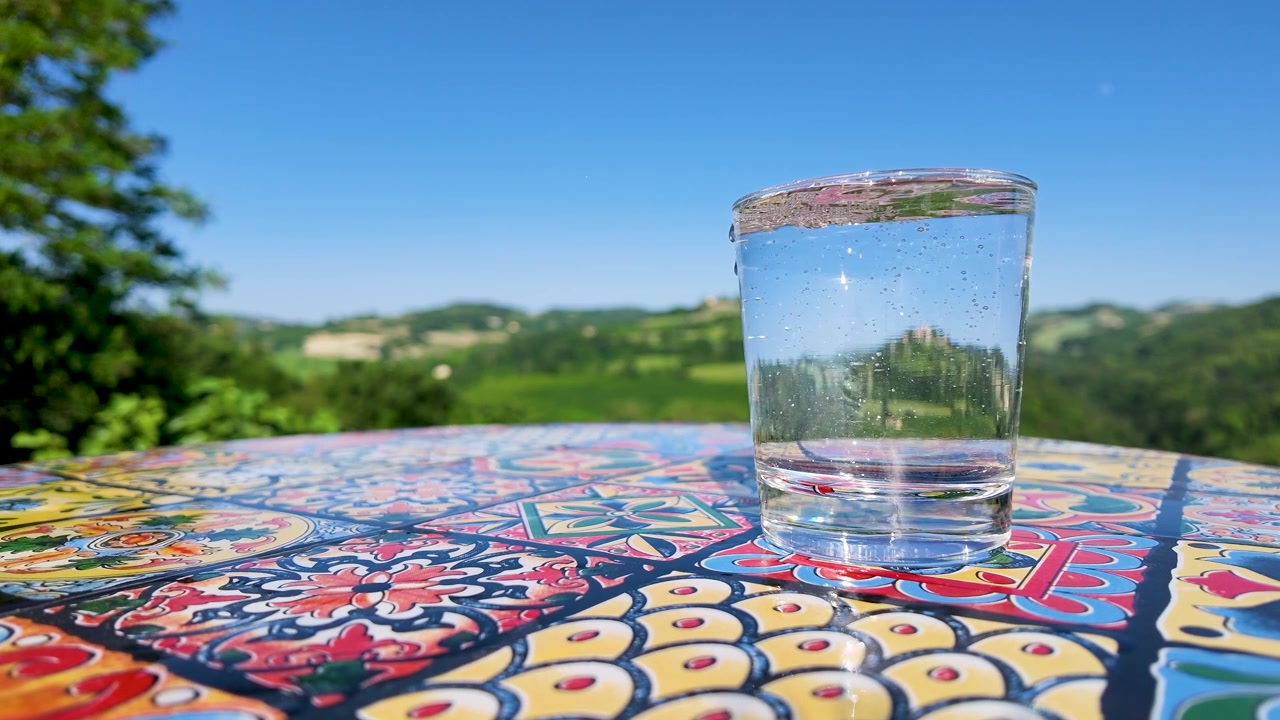 Bollicine di acqua frizzante in un bicchiere su un tavolo a mosaico con vista sulla campagna italiana.