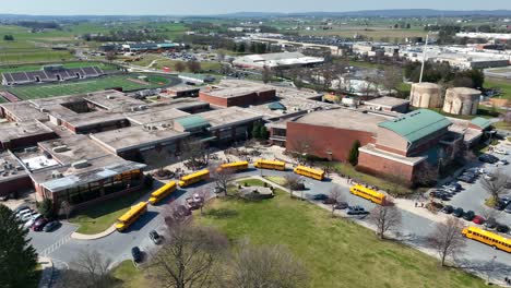 row of yellow school buses arriving at american school during sunny day