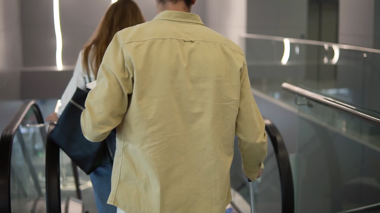 Rare view of caucasian family with yellow stylish suitcase going down by the escalator with their pretty daughter hold by