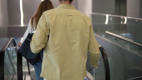 rare view of caucasian family with yellow stylish suitcase going down by the escalator with their pretty daughter hold by