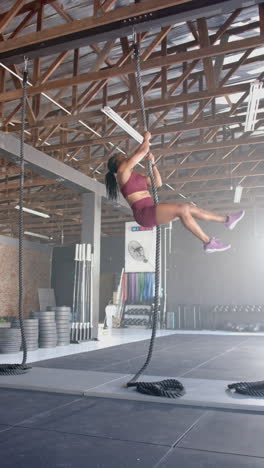 vertical video: climbing rope in gym, woman in athletic wear exercising upper body strength