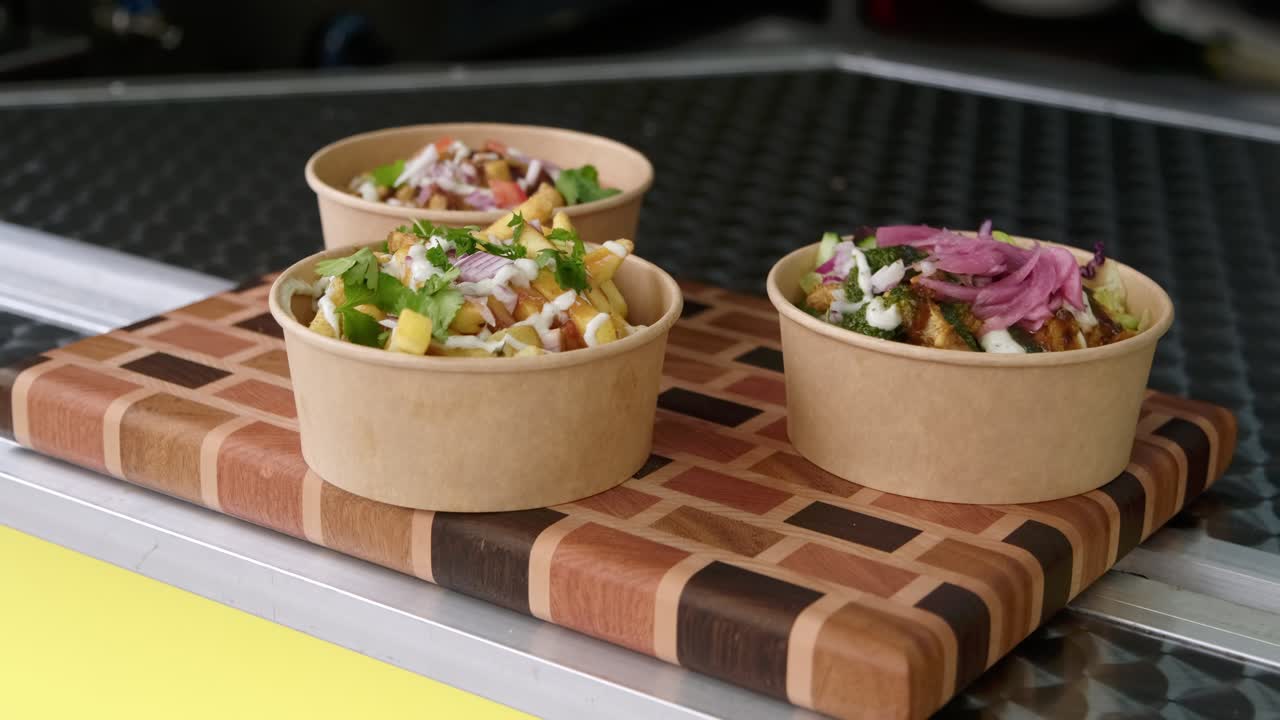 Medium shot of biodegradable poke bowl with Indian chicken tikka masala and other curry dishes ready for customer displayed at food truck with fries.