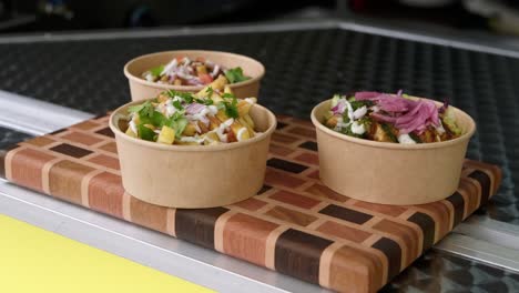 medium shot of biodegradable poke bowl with indian chicken tikka masala and other curry dishes ready for customer displayed at food truck with fries.