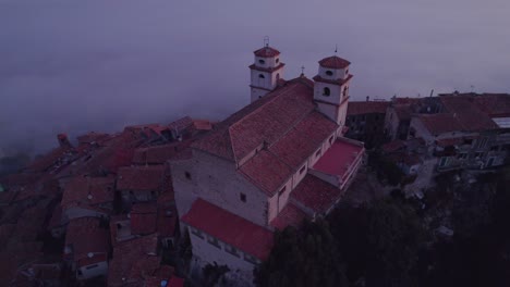 Church-on-top-of-hill-with-stunning-view-of-mist-filled-valley-at-sunrise,-aerial