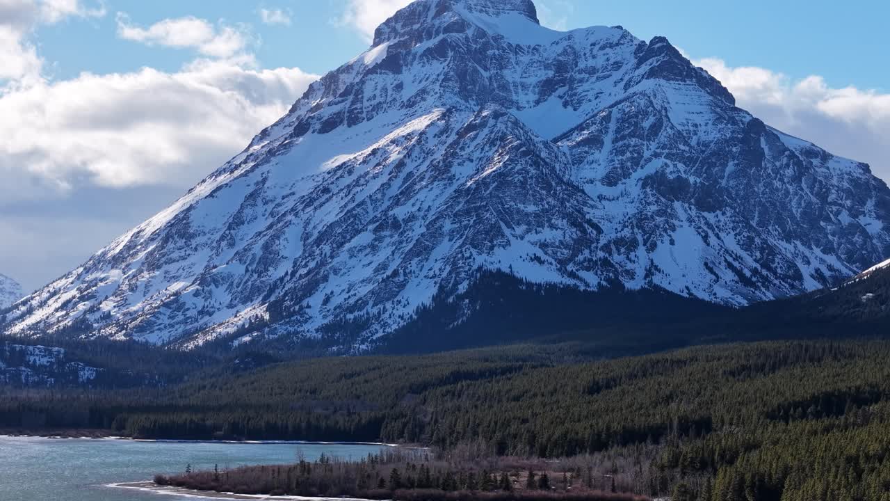 Vista aerea di un lago turchese circondato da una foresta di conifere e aspre montagne innevate in Montana