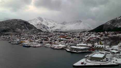 calm fjord and fishing village in skjervoy island in northern troms, norway with snowy alpine mountains in background on a dramatic winter day