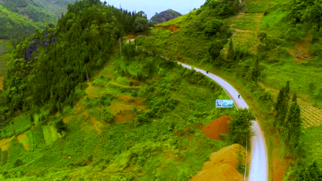 aerial dolly forward of a winding road cut into the mountainside of the misty mountains of the dong van karst plateau geopark