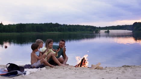 rodzina jedząca kiełbaski na plaży.