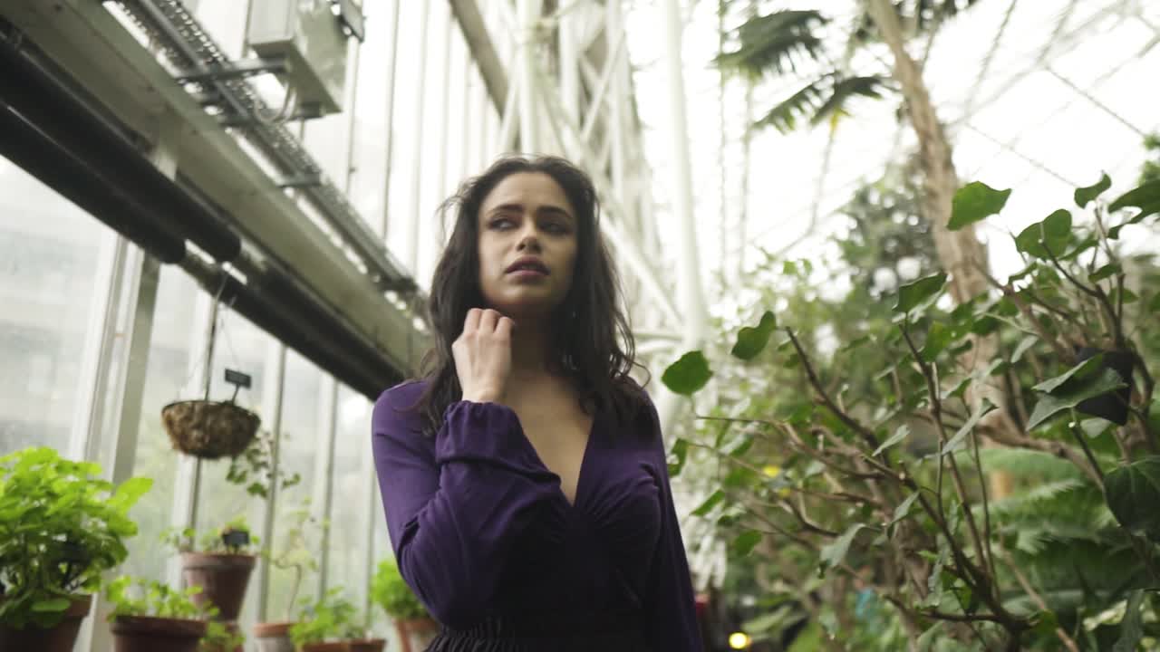 mujer joven del medio oriente caminando por el invernadero mirando la vegetación y fuera de la ventana