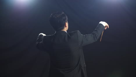 アジアの指揮者男がバトンを握り黒人スタジオでジェスチャーを示している後ろの景色