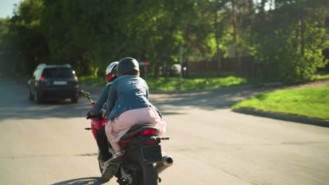 back view of two friends riding a power bike behind a black jeep and a white car seen ahead, the road is flanked by green trees and electric poles