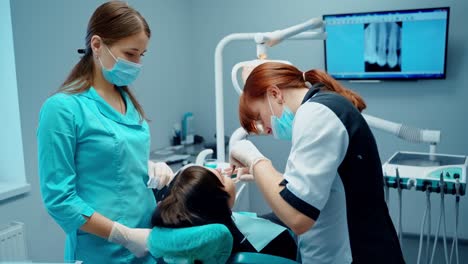 dental procedure in stomatology cabinet. patient sitting in dental chair while professional dentist and a nurse treating teeth.