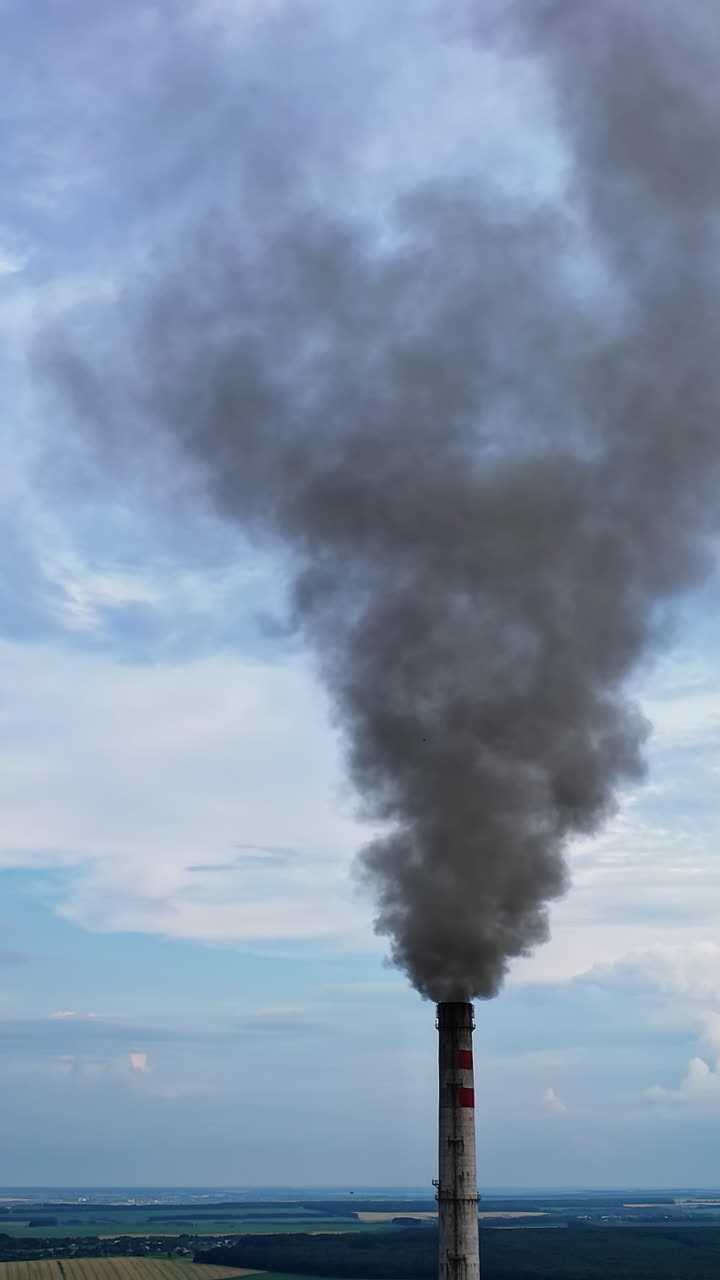 View from the drone at the old aged weathered tall industrial factory chimney with smoke over it. Cloudy sky background. Vertical video