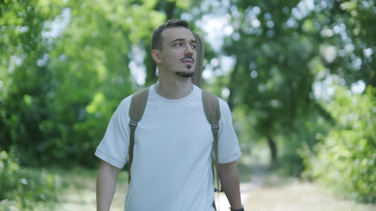 joven caminando con la guitarra en la calle cerca del bosque