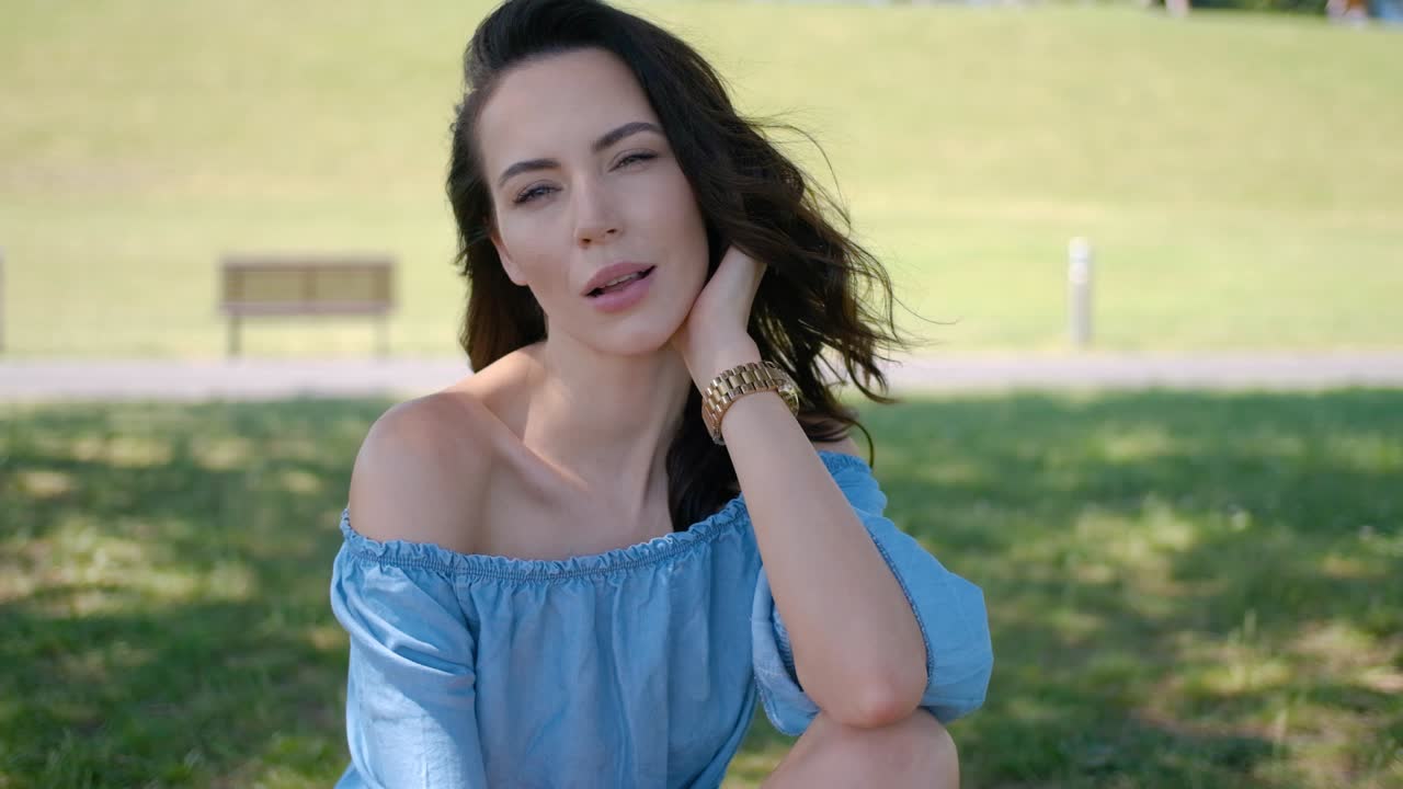 Bella modella con lunghi capelli castani seduta sull'erba verde