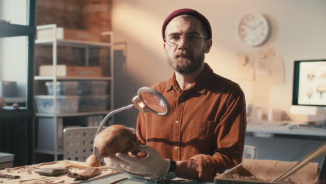 portrait of archaeologist in gloves holding skull at desk in laboratory