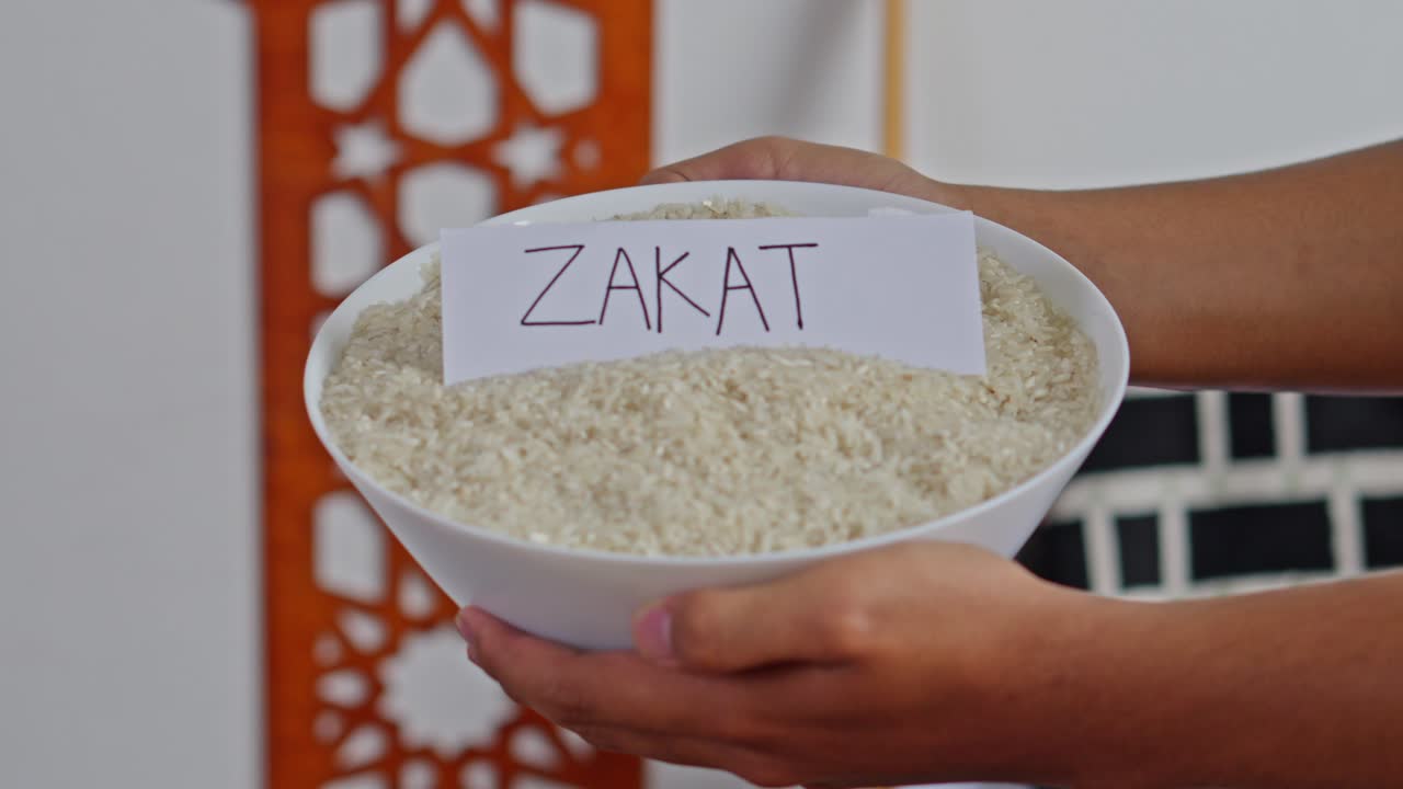 Hands holding white bowl of rice with "ZAKAT" label representing Islamic alms giving and charity
