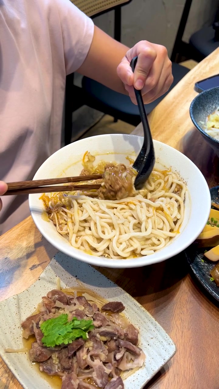 Primo piano di mani che mescolano noodles e carne di maiale macinata in una ciotola bianca in un ristorante.