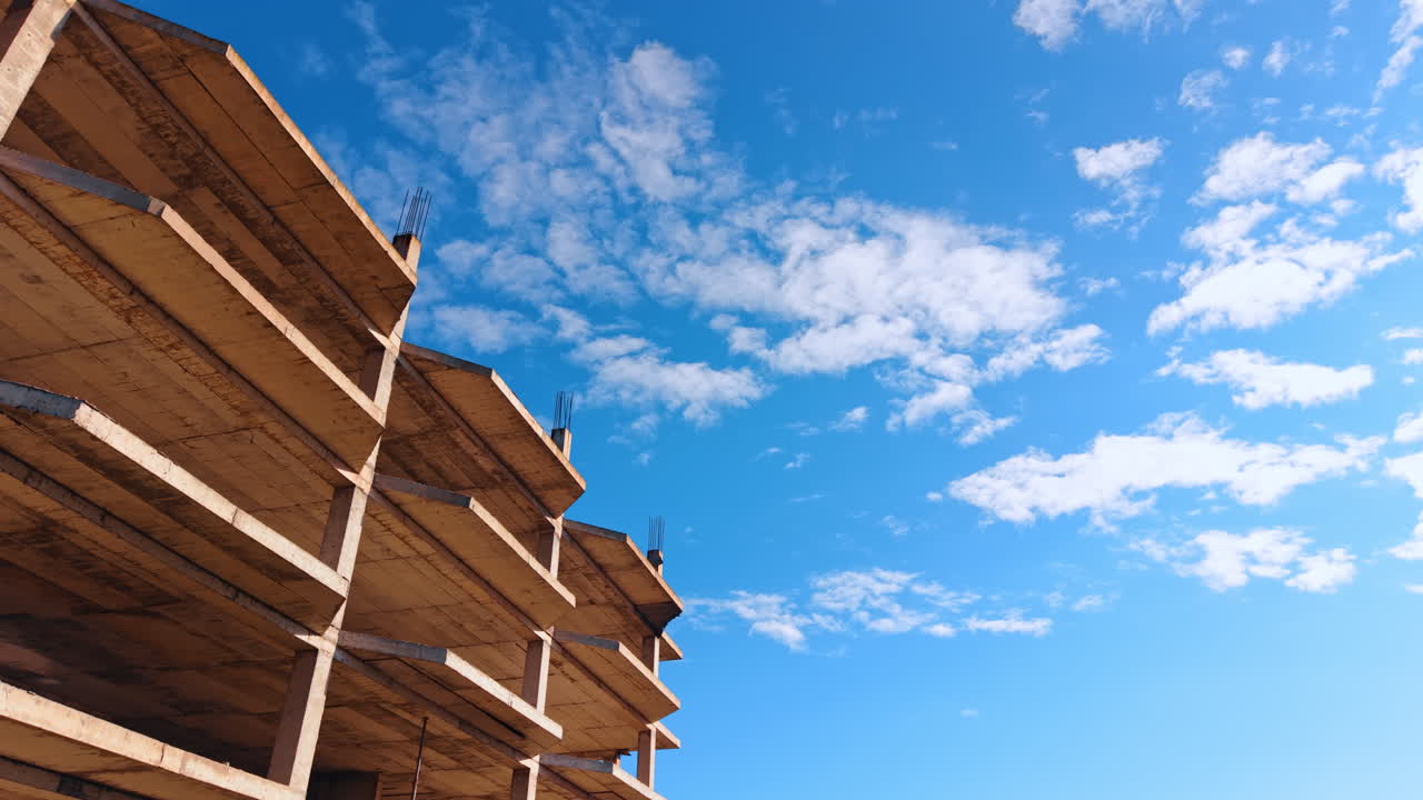 Volo sull'esterno incompiuto di un edificio a più piani. Cielo blu con nuvole bianche e leggere sullo sfondo.