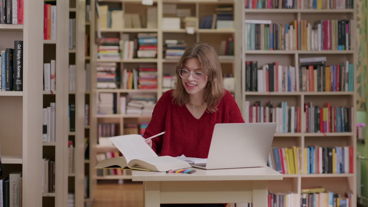 estudiante caucásico con gafas investigando en la biblioteca usando una computadora portátil