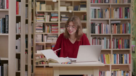 estudiante caucásico con gafas investigando en la biblioteca usando una computadora portátil
