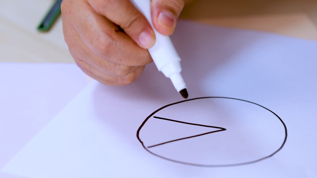 Close-up of hand sketching pie chart slice on white paper with black marker, natural lighting