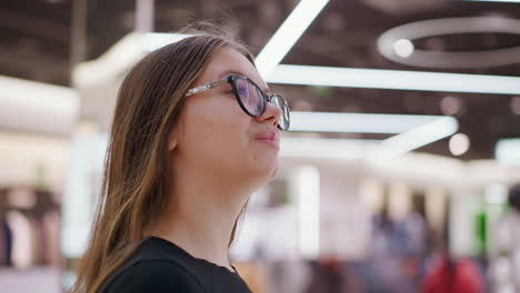 joven caminando con confianza por el centro comercial, usando gafas con fondo borroso de la tienda y figuras indistintas, mostrando un entorno de compras moderno y una experiencia de compras de moda