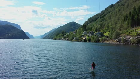woman riding spectacular tall swing with norwegian fjord veafjord in background - aerial showing woman dangling her feet down into sea surface surrounded by stunning scenery - norway