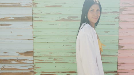 Portrait-of-smiling-hispanic-woman-in-front-of-weathered-wooden-wall-in-sun,-copy-space,-slow-motion