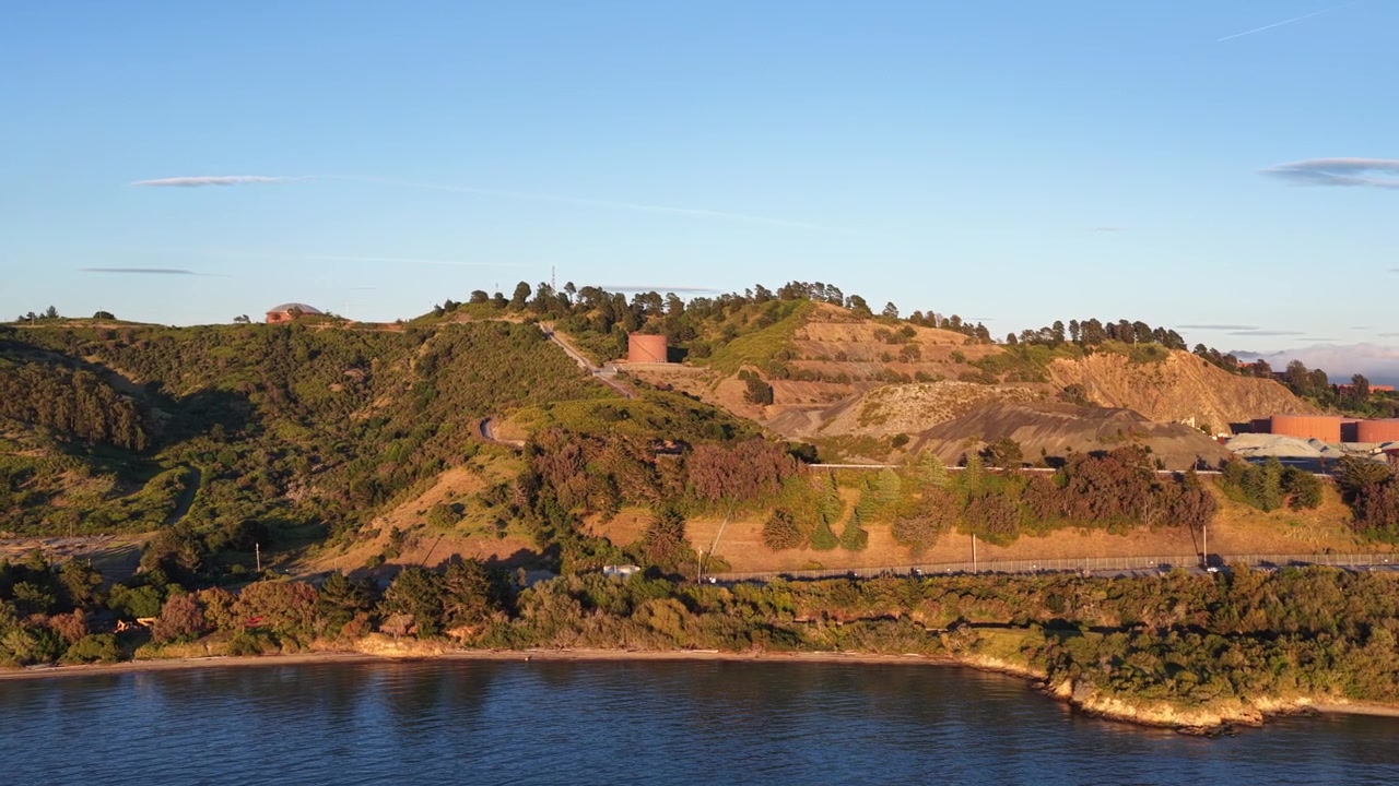 Riprese aeree all'ora d'oro che mostrano la costa panoramica e le lussureggianti colline verdi di Point Richmond in California, con le acque calme della baia di San Francisco sotto un cielo azzurro e limpido al tramonto