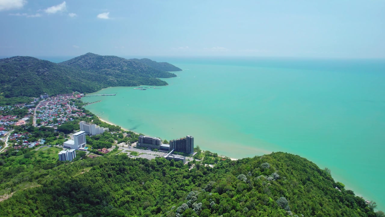 Cảnh quay drone điện ảnh bay qua một ngọn núi rừng xanh tươi để hé lộ một thị trấn ven biển và biển xanh ngọc rộng lớn dọc theo Đảo Penang, Malaysia.