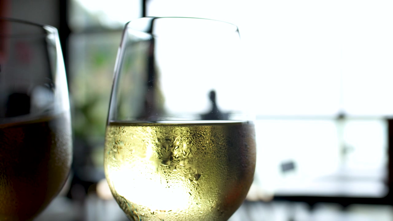 Primo piano di un bicchiere di vino bianco freddo con goccioline d'acqua su un tavolo all'aperto.