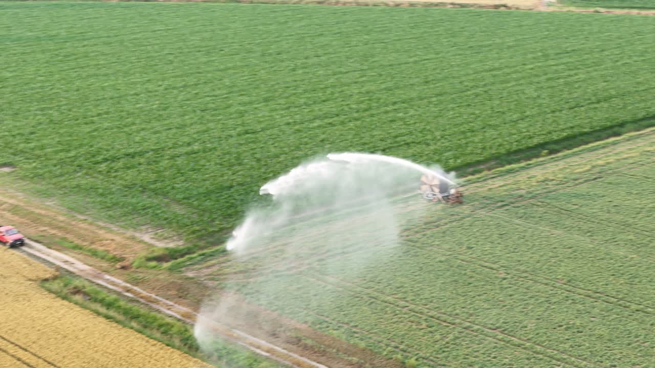 Agricultural machinery irrigating soybean crops with rain gun in Po Valley, Italy, during spring season, creating a refreshing and vital scene, slow motion drone shot
