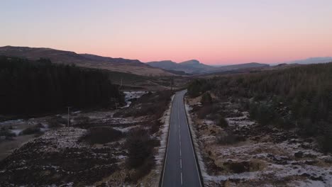 twilight over a solitary road through rugged terrain, snow patches, serene landscape, aerial view