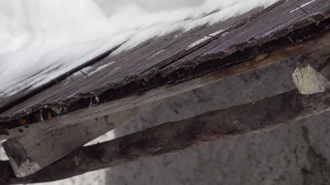 Snow is melting and its water is trickling down from a wooden roof