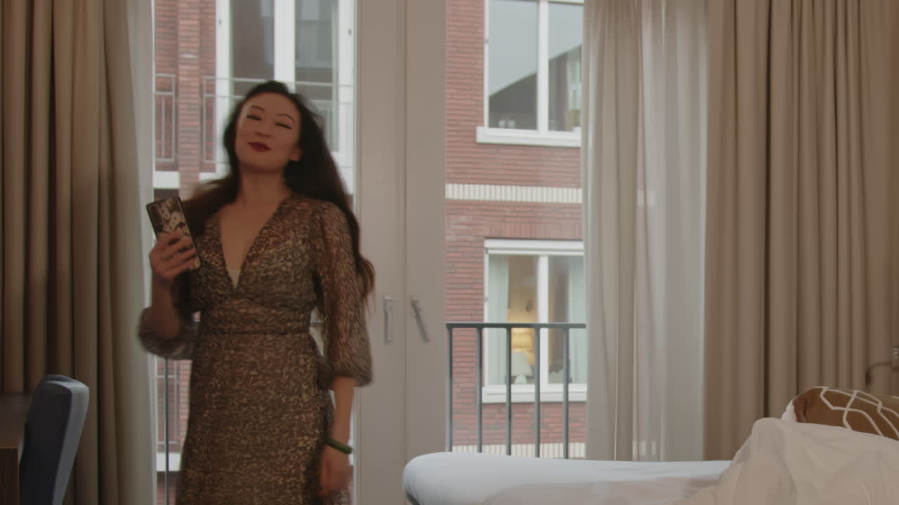 An attractive woman in a hotel bedroom makes a photo with her cellphone and walks away smiling