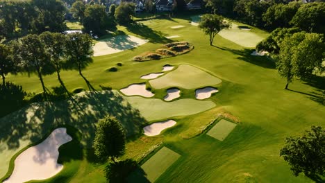 an aerial drone shot of a beautiful golf hole during sunrise showing the fairway, green, and bunkers, accompanied by long shadows from the trees