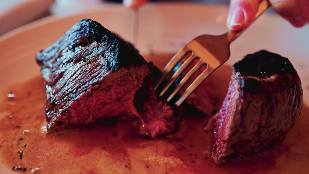 Close up of a knife slicing through a medium rare steak, exposing its tender, juicy interior